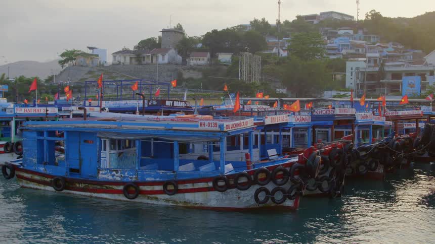 A row of identical colorful boats flying vietnamese flags docked on the coast of a land mass