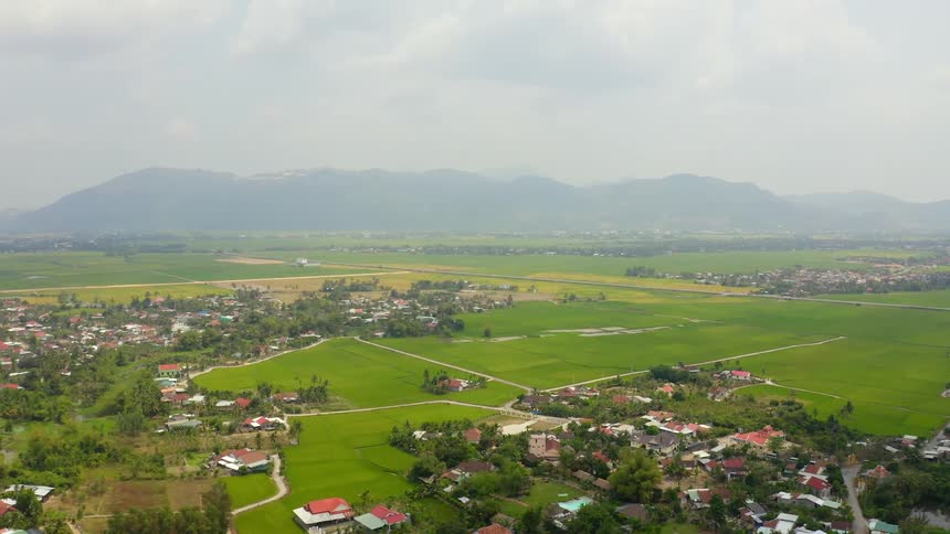 Dense neighborhoods are separated by lush green fields in a town below a mountain range