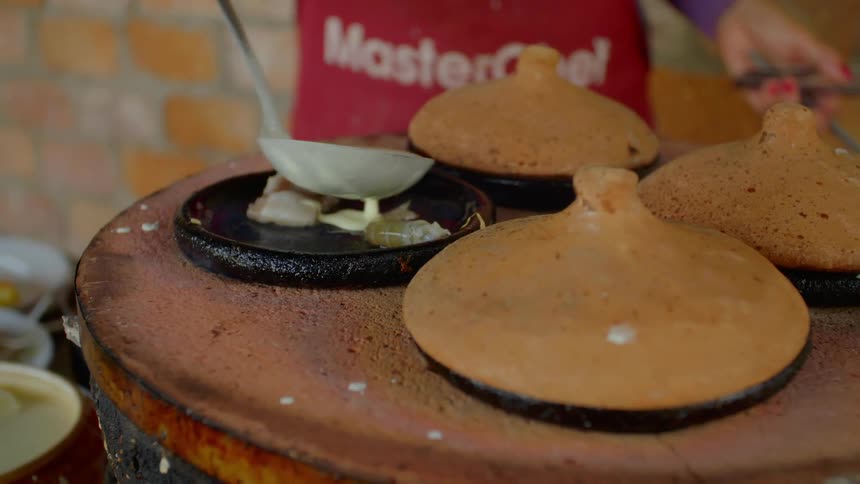 A man uses a ladle to pour sauce over shrimp lying on the ceramic cooking surface of a traditional stove
