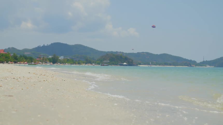 Waves rolling in to the shore and parasails flying in the far distance