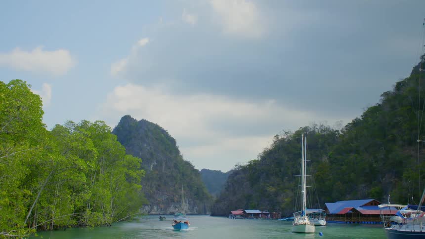 Boats travel along a bay surrounding by mountains and forest on a sunny day