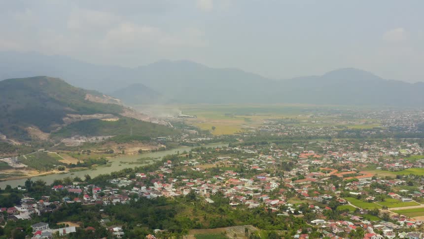 A town next to a pale green river below low mountains shrouded in fog