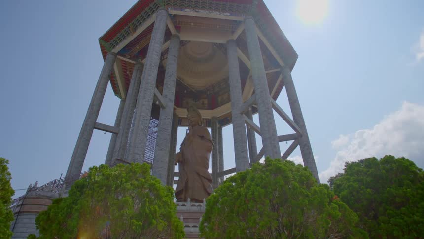 A sculpture of a standing buddha sits in a gazebo on top of a brick structure outdoors