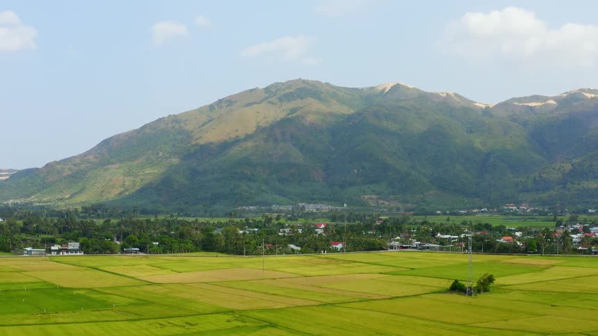 A grassy plain with trees buildings a mountain range and the sky in the background