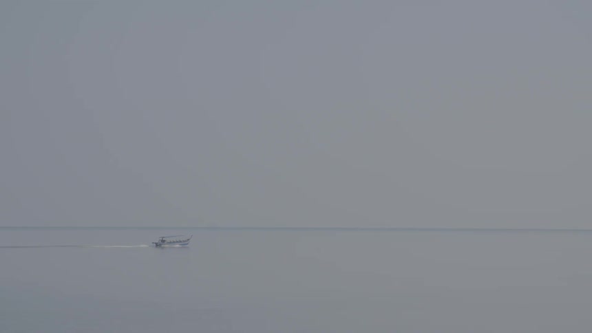 A boat travels on a body of water through thick fog