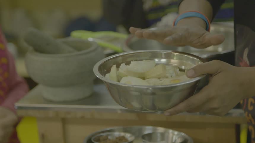A person holding a bowl with food with a table in the background