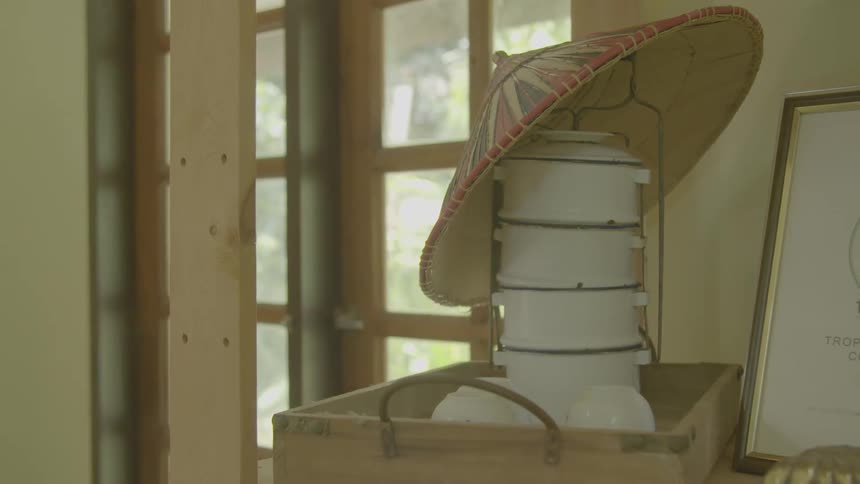 White pots and a conical asian hat sit on a decorative wooden tray near the front door of a house