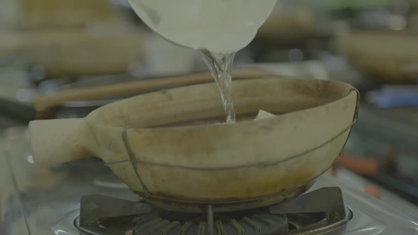 Water is poured from a pitcher into an odd shaped pot on a stove
