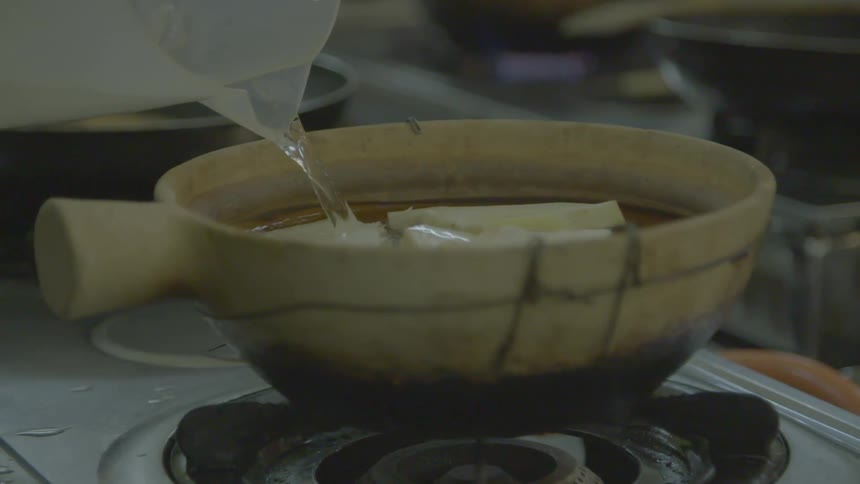 Water being poured into a pot of cooking food on a stovetop