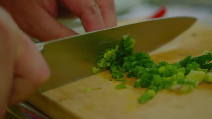 A knife chopping vegetables on a wood cutting board