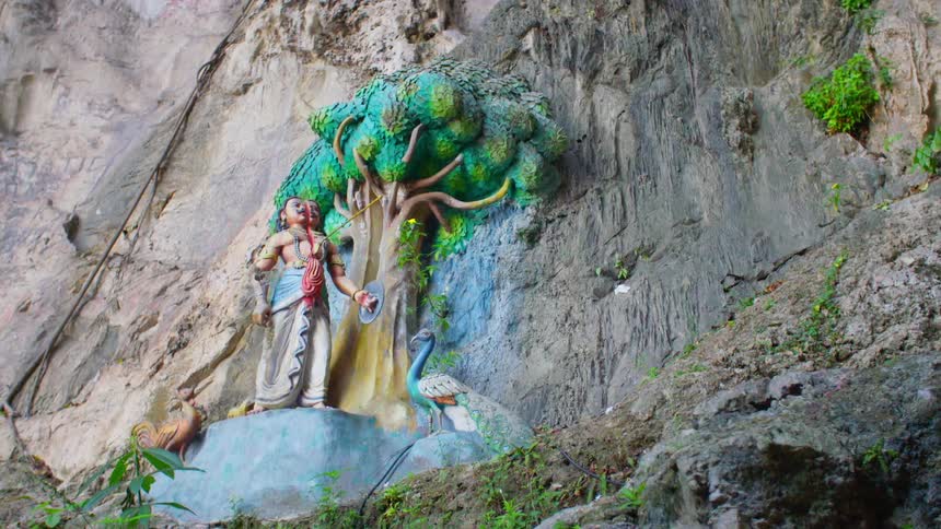 A statue of a tree human and peacock stand next to a rocky cliff