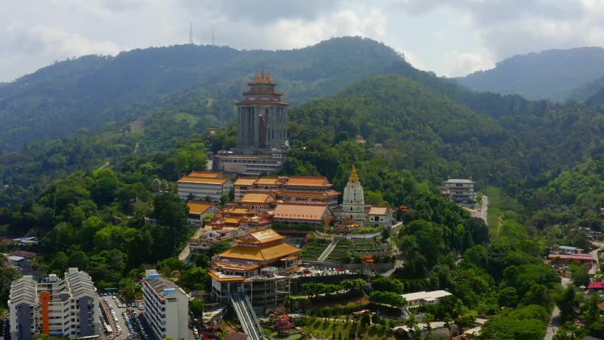 A large monument sits up on a hill overlooking a city near tree covered mountains