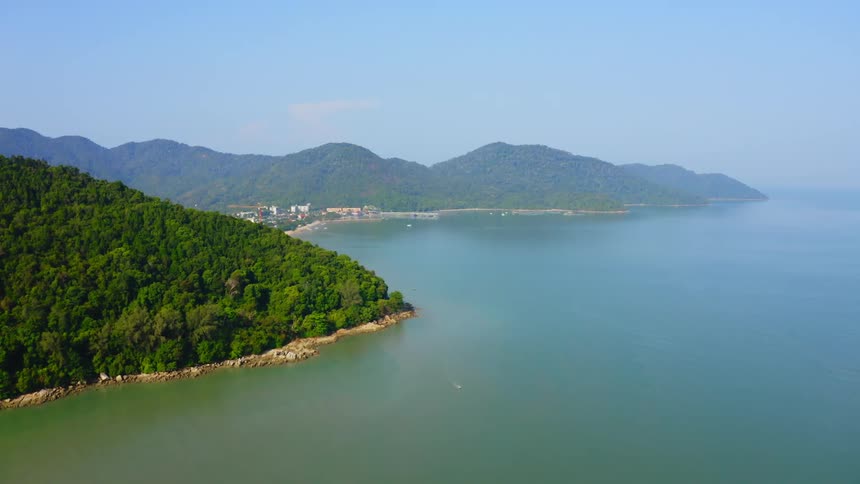 A city on the coast of a bay at the base of mountains covered in forest and fog