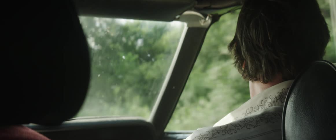 A young man sitting in a car as it drives past a forest