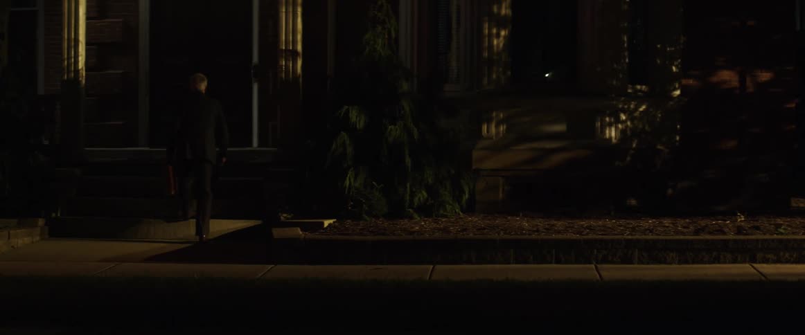 A man walks briskly on a city street holding a briefcase and walks into house