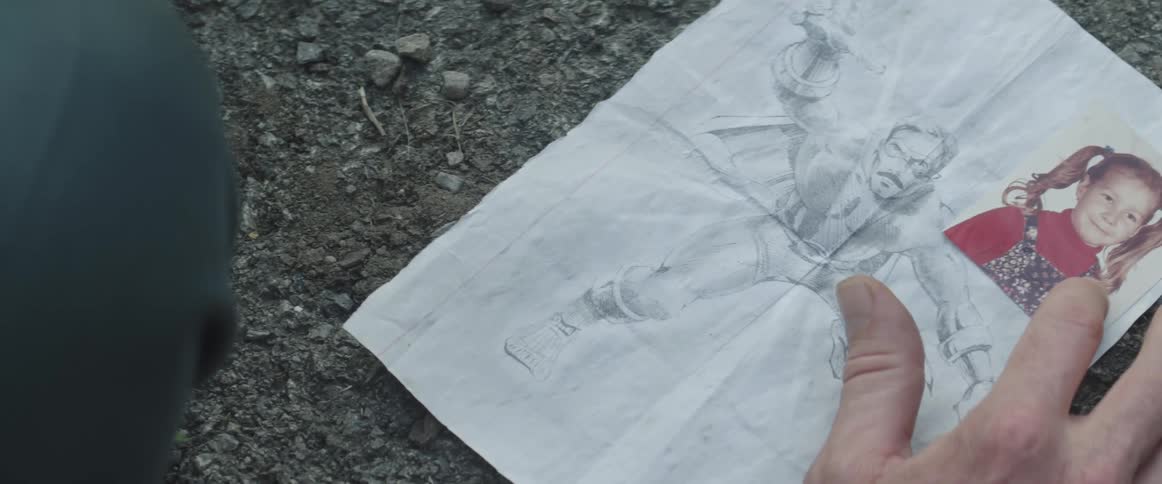 Person places photograph of young girl on pen and pencil drawing set on ground