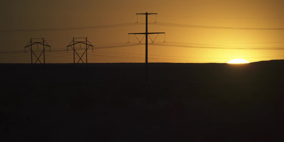 The sun is setting in the horizon past power lines