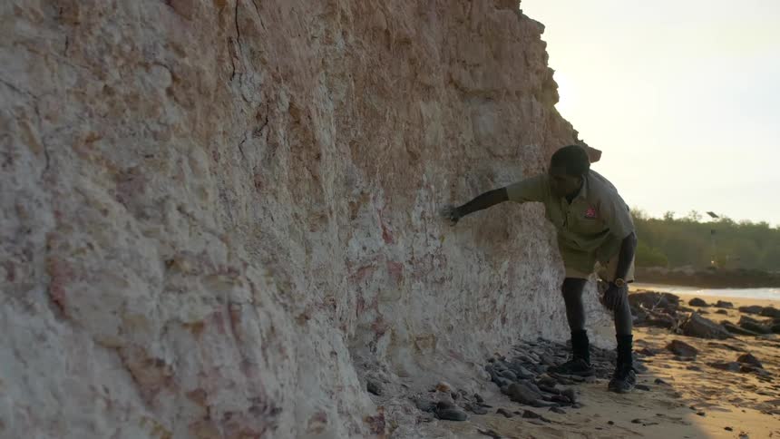 An aboriginal man placing his hand on white ochre rock wall