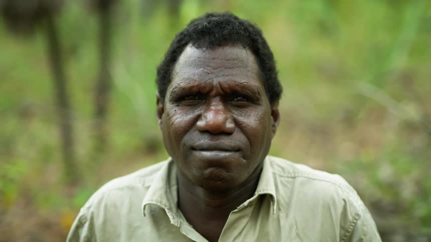 An aboriginal man outside looks ahead and smiles