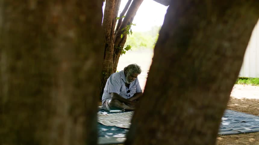 A man sitting outside on a blanket painting