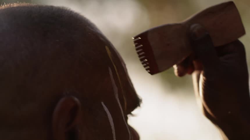A hand holding a clay comb to apply texture to a sculpted face