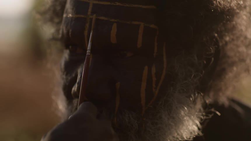 Close up of a senior aboriginal australian painting his face with a small brush