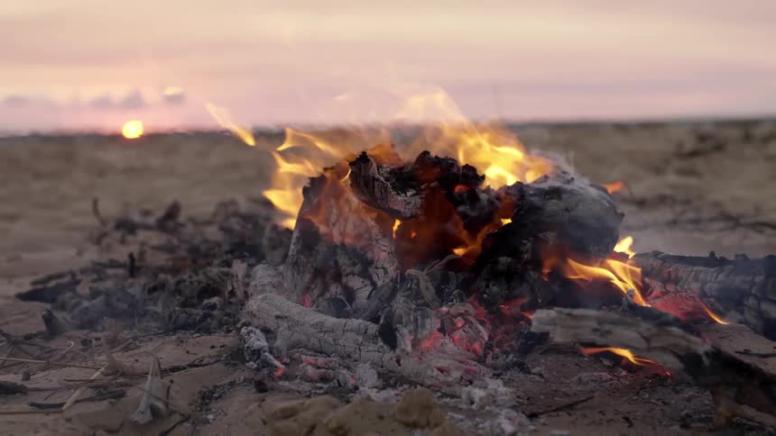 A campfire with flames and smoke with the sky and sunset in the background