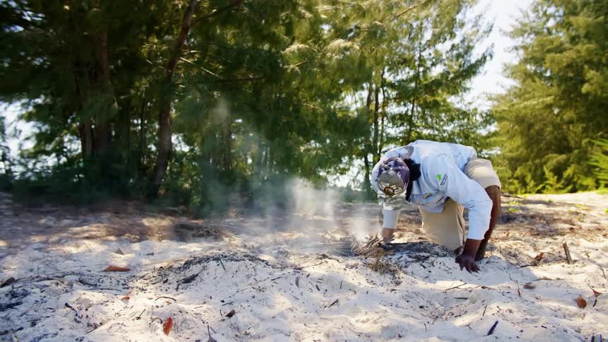 A man kneels to on a small campfire in the sand