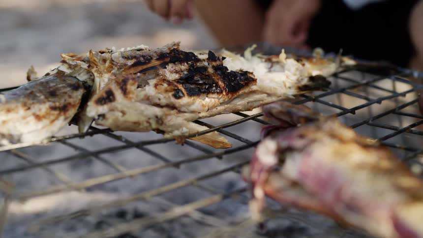 A man outside picks a piece of fish off of a grill