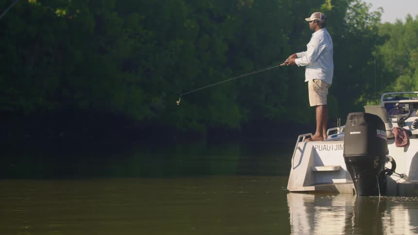 Man stands on edge of boat casting line into water