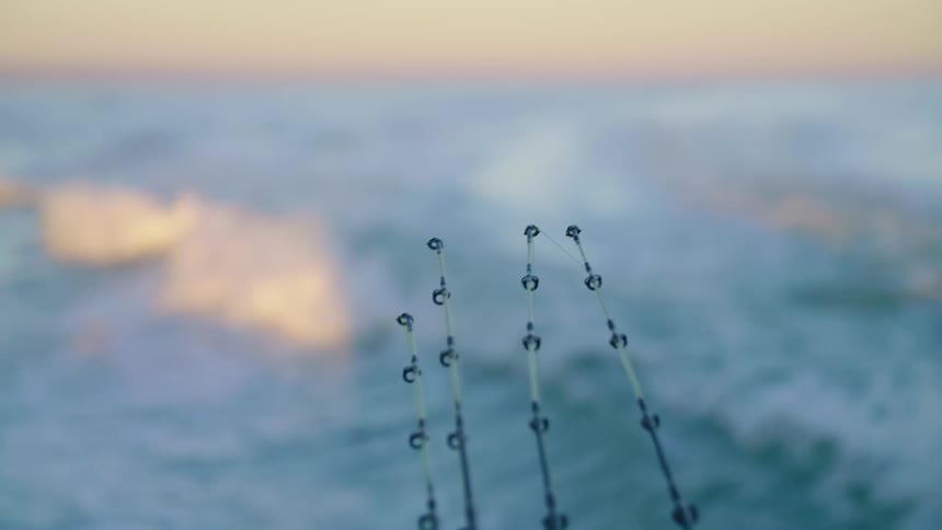 A group of fishing poles on a boat as it travels across the ocean waves in the evening