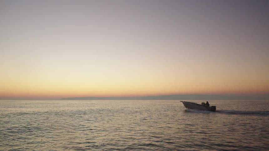 Person driving speedboat on ocean at sunset