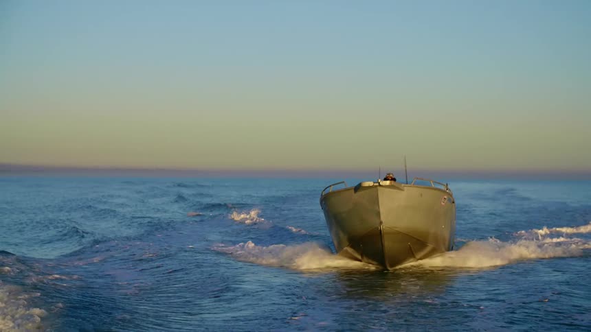Man pilots boat through ocean waves as horizon remains slightly pink