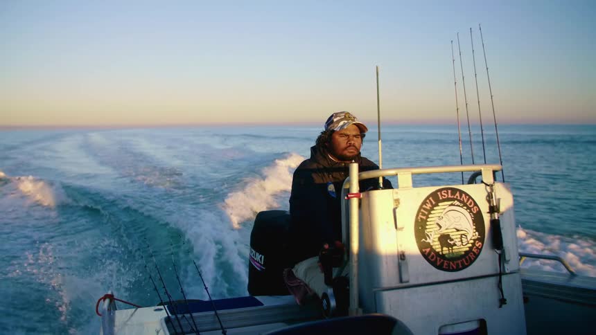 An employee for a fishing boat company sails the boat through the ocean at sunset