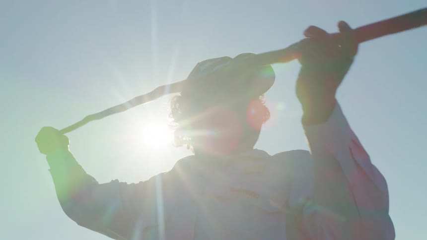 A man throws a fishing spear while standing under the glaring sun