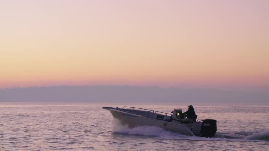 Boat traveling on the sea is silhouetted against the red sky