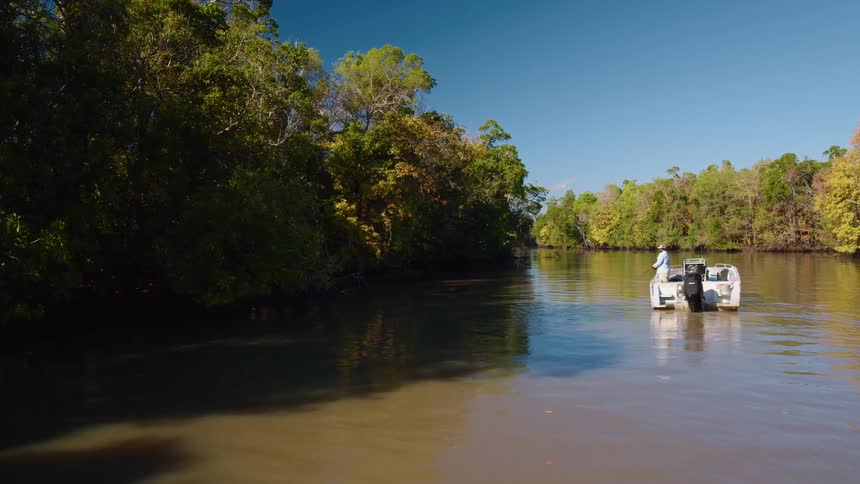 A man that is fishing on a river in a boat