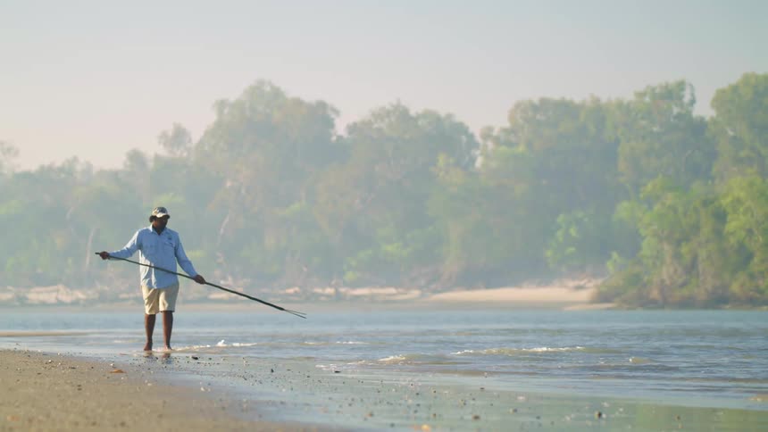 A man walking along the edge of a river with a fishing neck