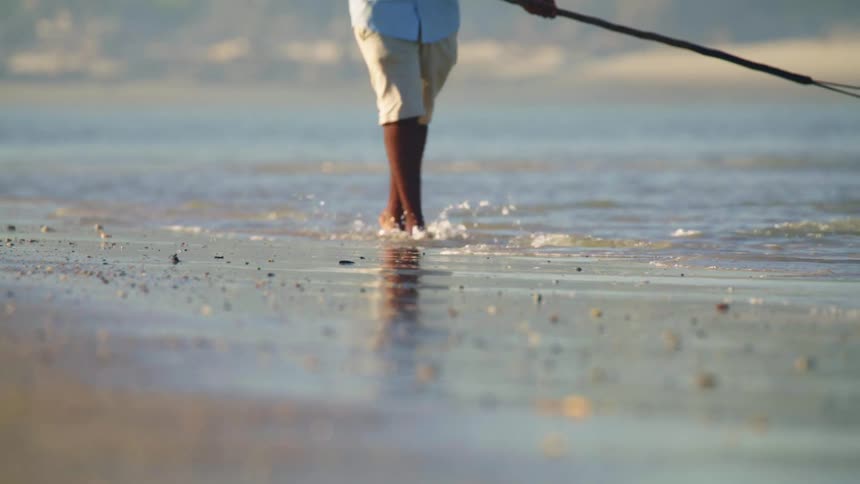 A man walks on the shore with a rod for spear fishing