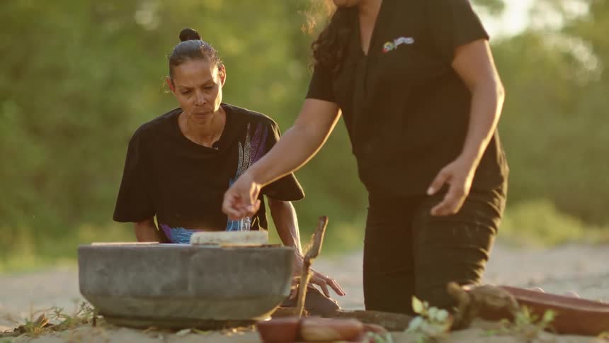 Two women are cooking on a stone grill outside