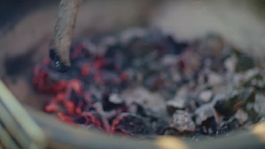 A stick stirs coals in a fire