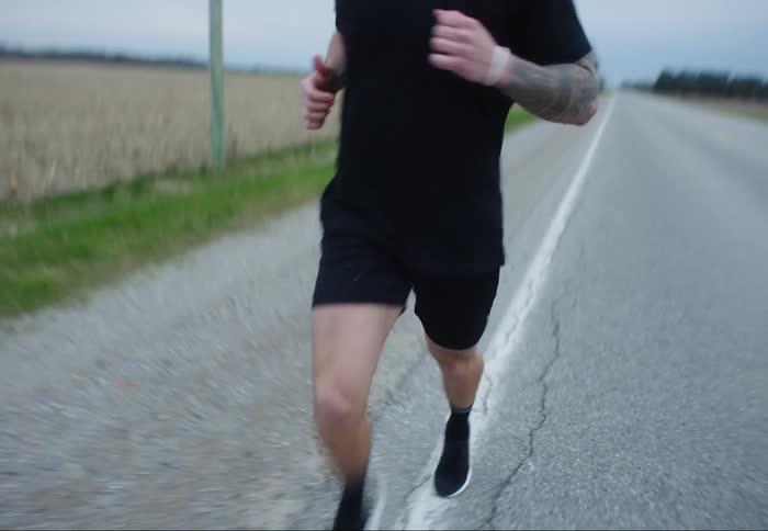 A young man runs down a road next to a field