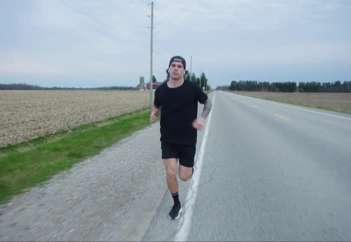 A man wearing earbuds jogs down the side of a road in the countryside