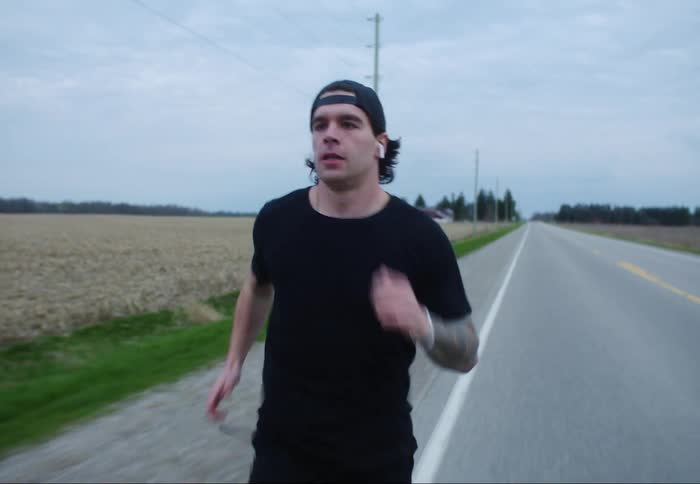 A man runs on the shoulder of a rural road by a large field