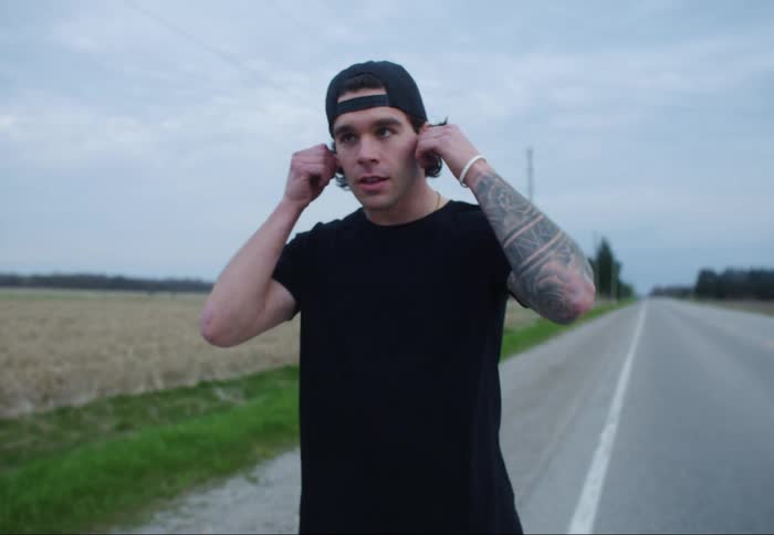 Man puts in earbuds to and then takes off on his run on a rural road