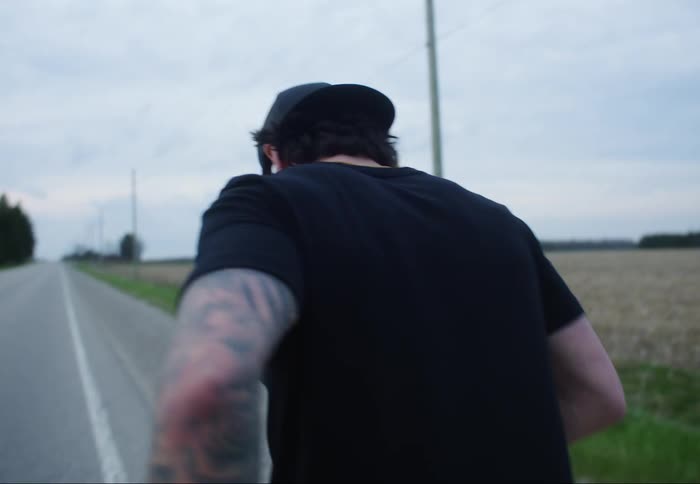 A man sticks a pair of earbuds in his ears before beginning to jog down the side of a road
