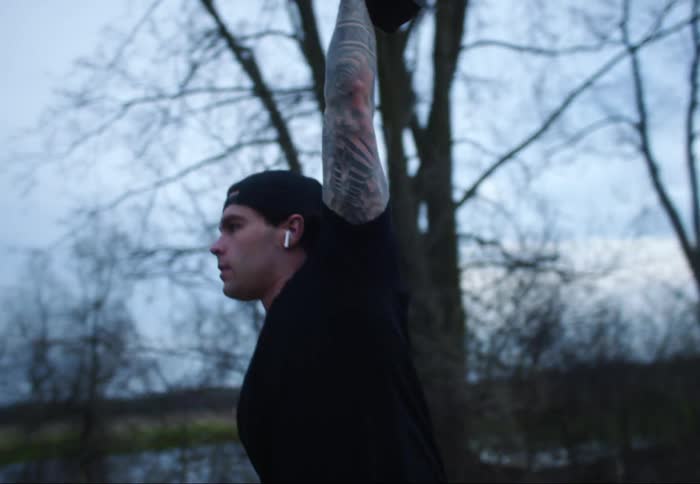 A man lifts a weight high in the air and then drops it back down to the ground standing on a dirt rural road
