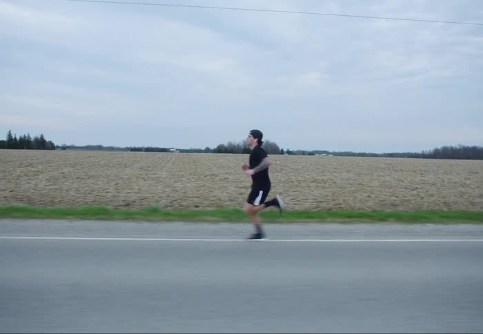 A person runs on a rural roadway next to a field