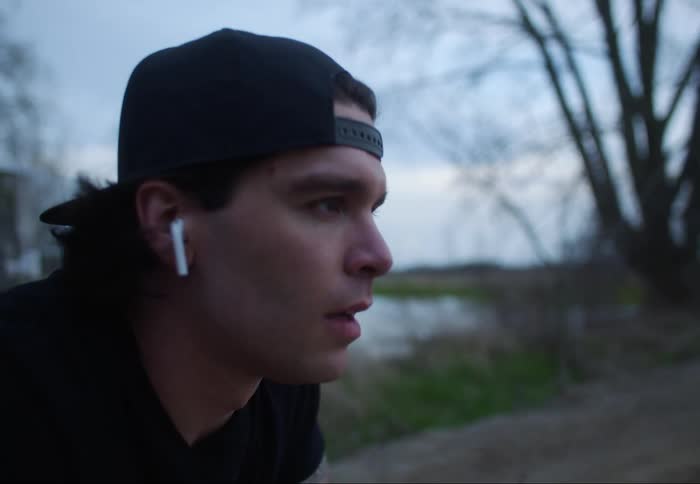 A young man is squatting in the middle of a dirt road while breathing heavily on a cloudy fall evening