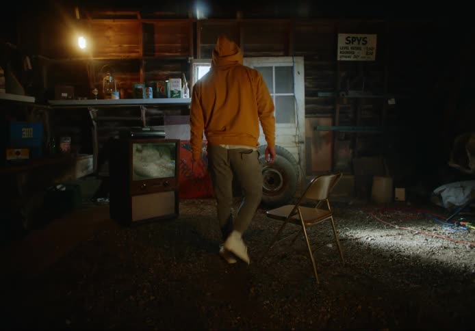 Man sits down on metal folding chair in barn in front of old television set